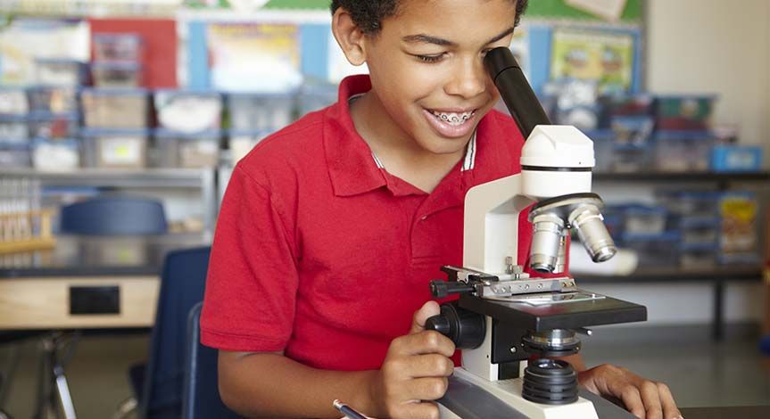 Boy in red shirt looking though a microscope in a classroom