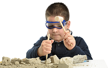 Boy wearing safety goggles breaking rocks with hammer and pick