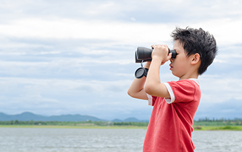 Boy in a field looking through binoculars